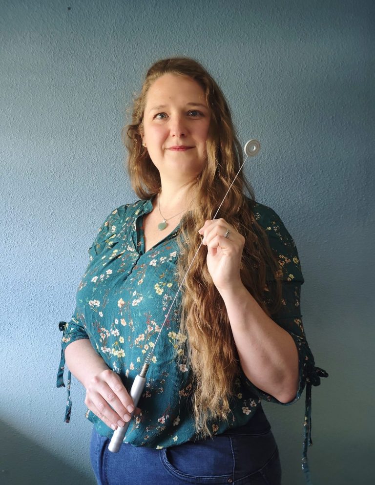 Eigenaar en oprichtster van MAGG Coaching Michelle Groothoff Vrouw met lang, golvend haar, draagt een groene blouse en houdt een toverstaf vast.